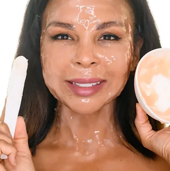 Woman applying a facial mask with a brush and container on a white background