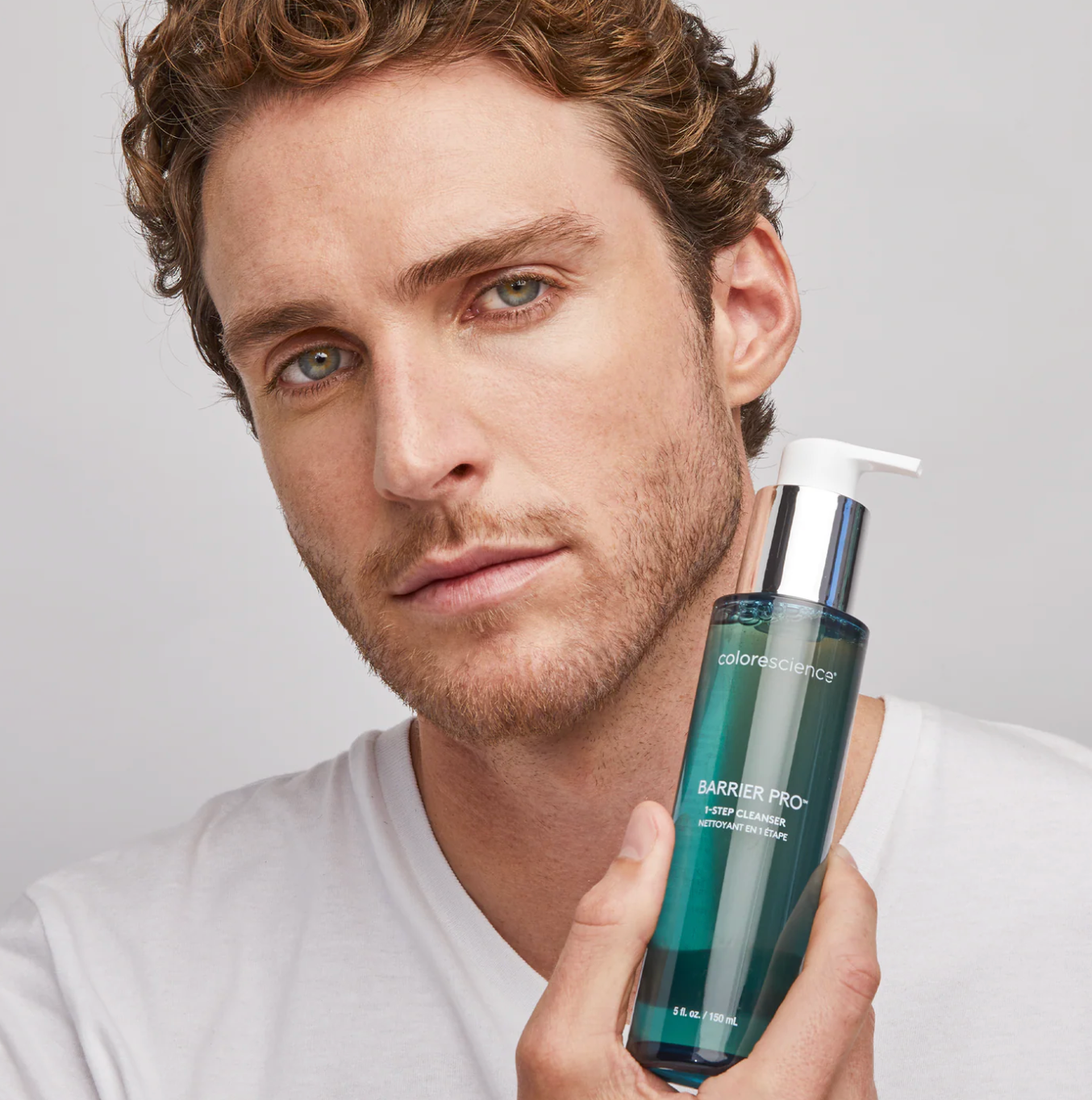 Man holding a bottle of Colorescense Barrier Pro skincare product against a neutral background