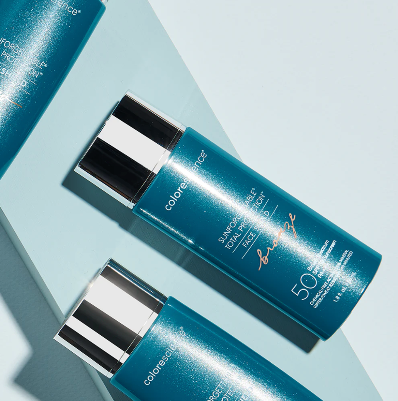 Two blue sunscreen bottles with silver caps on a light blue background