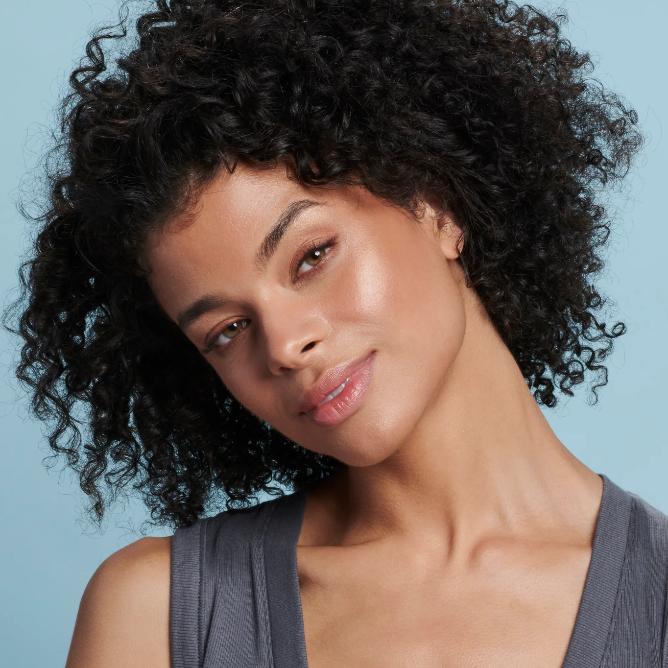 Woman with curly hair wearing a gray top against a light blue background