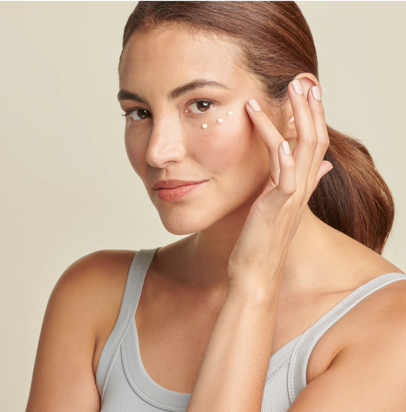 Woman applying cream to her face with a neutral background