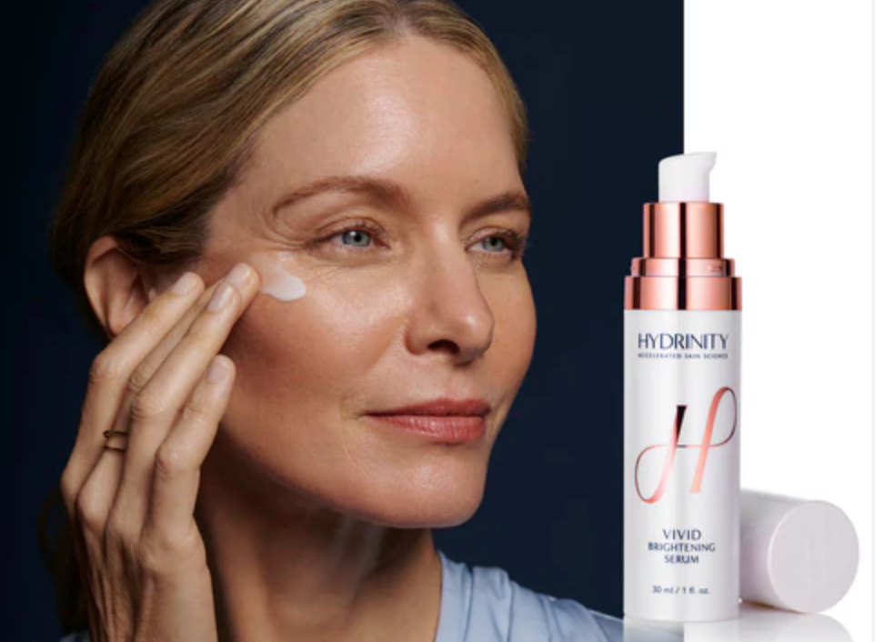 Woman applying skincare product to face with Hydrnity serum bottle in the background