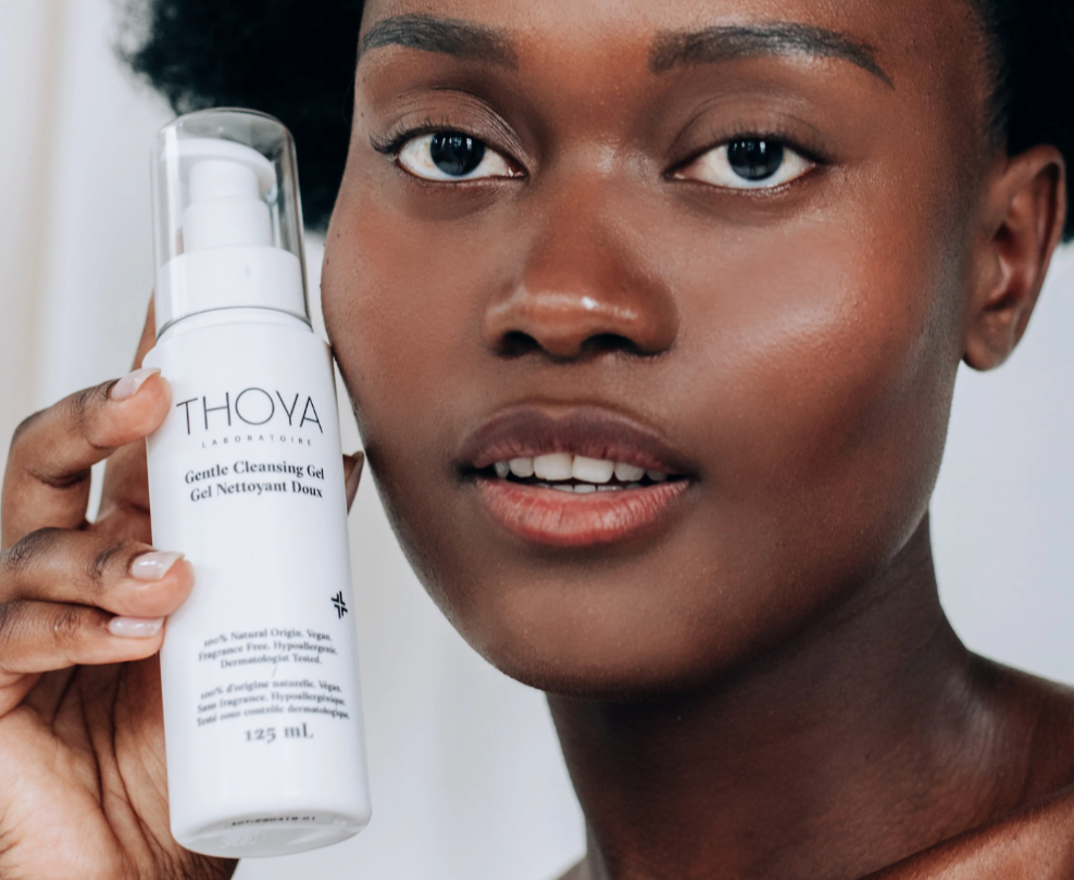 Woman holding a Thoya skincare product with a neutral background