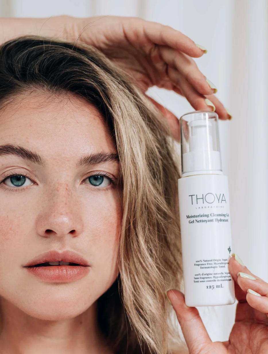 Woman holding a bottle of THOVA skincare product close to her face.