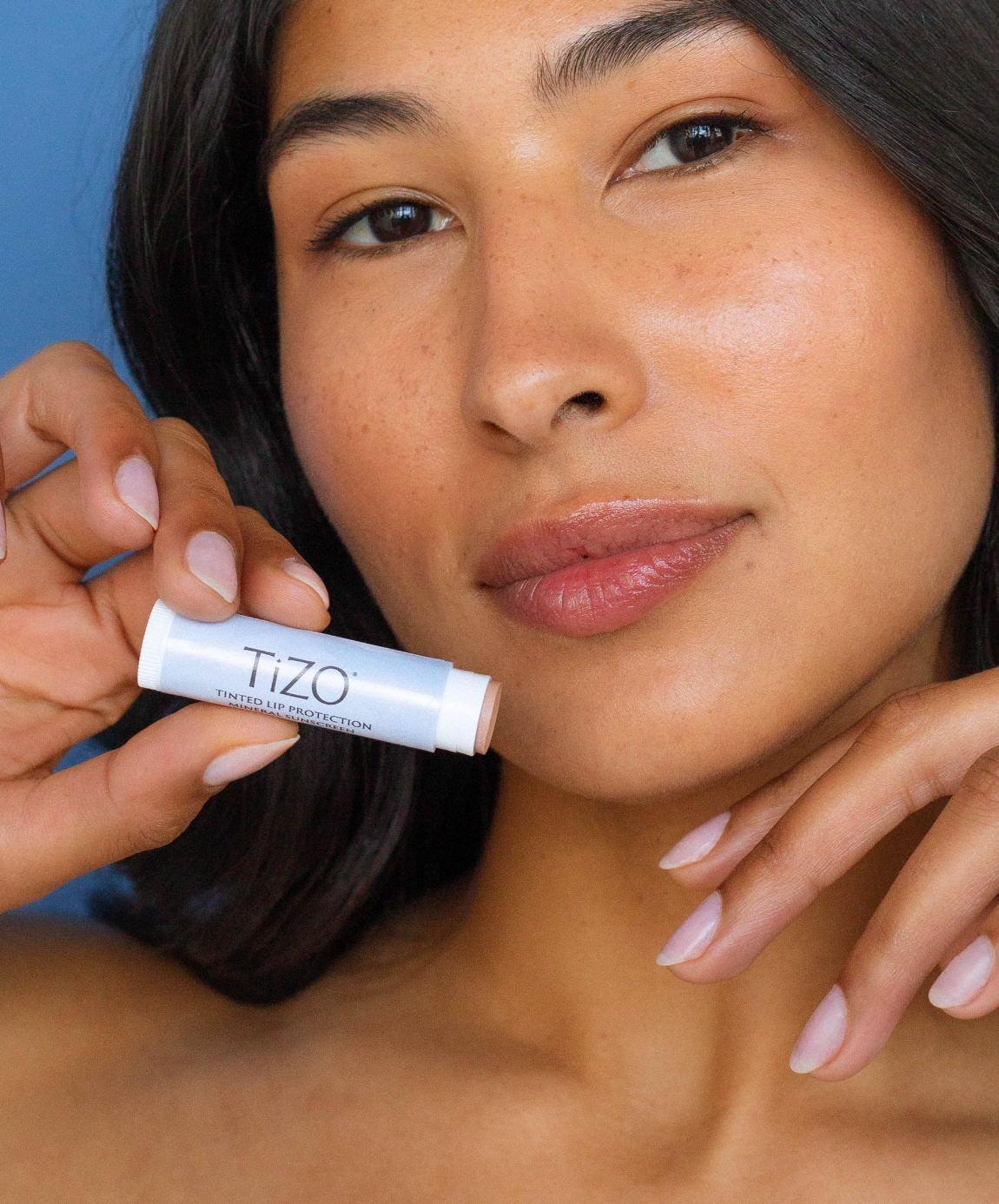 Woman holding a TIZO lip balm stick against a blue background