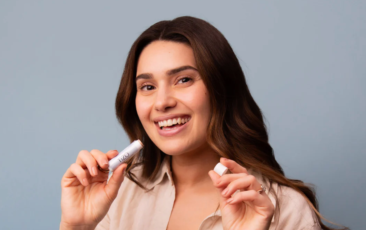 Woman holding two small white bottles against a gray background